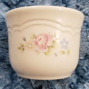 May include: A white ceramic bowl with a floral design featuring pink, yellow, and blue flowers. The bowl has a scalloped rim and a smooth, glossy finish.