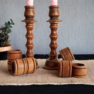 May include: Two wooden candle holders with a set of six wooden napkin rings. The candle holders are brown and have a fluted design. The napkin rings are also brown and have a simple design.