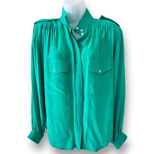 May include: A long-sleeved, emerald green blouse with a high collar, button closure, and two flap pockets.