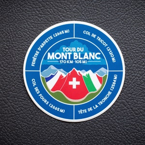 Könnte beinhalten: Ein blauer und weißer runder Aufkleber mit dem Text "Tour du Mont Blanc 170 KM - 105 MI" und einer Grafik einer Bergkette mit einer Schweizer Flagge. Der Aufkleber enthält auch die Namen von vier Bergpässen: "Fenêtre d'Arpette (2665 M)", "Col des Fours (2665 M)", "Tête de la Tronche (2584 M)" und "Col de Tricot (2120 M)".
