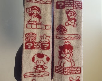 May include: A white knitted scarf with red pixelated images of a video game character. The images include the character jumping, running, and collecting coins.