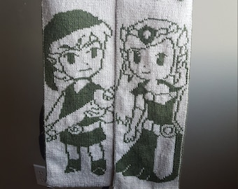 May include: A white knitted scarf with green knit designs of Link and Zelda from the Legend of Zelda video game series. The scarf also has the text "Hey Listen!" and three hearts.