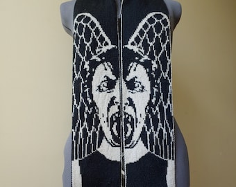 May include: Black and white knitted scarf with a graphic of a face with wings. The face is screaming with its mouth open.