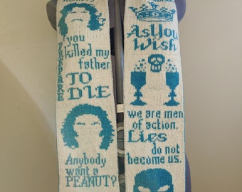 May include: A white knitted scarf with teal blue text and images. The text includes quotes from the movie "The Princess Bride" such as "As you wish", "Anybody want a peanut?", "Drop your sword", and "We are men of action. Lies do not become us."
