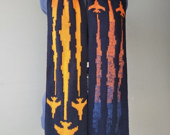 May include: A black knitted scarf with orange and blue stripes featuring a repeating pattern of airplanes.