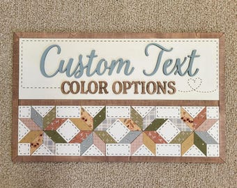 May include: Wooden sign with the words "Custom Text" in blue script and "Color Options" in brown block letters. The sign features a patchwork quilt design in various colors and patterns, with a light brown border.