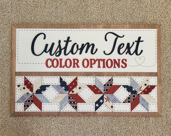 May include: Wooden sign with the words "Custom Text COLOR OPTIONS" in navy and red. The bottom section features a star quilt pattern in red, white, and blue. The sign has a brown wooden frame.