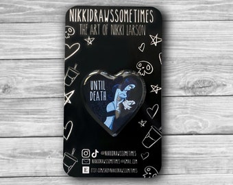 May include: A heart-shaped pin featuring a blue illustration of a couple with the text "UNTIL DEATH." The pin is on a black backing with white doodles and the text "NIKKIDRAWSSOMETIMES THE ART OF NIKKI LARSON."