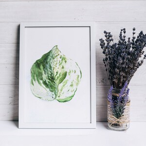 May include: A white framed watercolor painting of a single green and white leaf. The painting is on a white wooden background with a vase of lavender flowers to the right.
