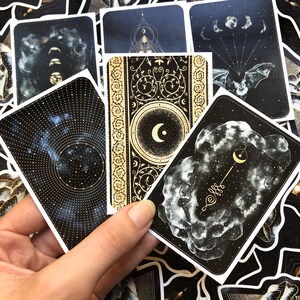May include: A set of ten black and gold stickers with celestial and moon designs. The stickers feature intricate patterns, stars, and moons.