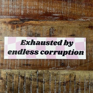 May include: A rectangular sticker featuring a light pink and white checkered pattern background with the black text "Exhausted by endless corruption" printed in a bold, serif font across the center of the design.