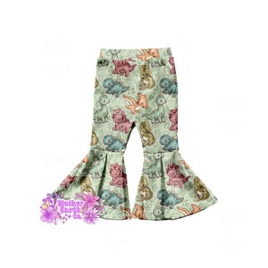 May include: Light green bell-bottom pants featuring an all-over print of various dinosaurs in shades of teal, brown, and orange. The fabric displays a repeating pattern of cartoon-style prehistoric creatures and foliage on a pale green background.