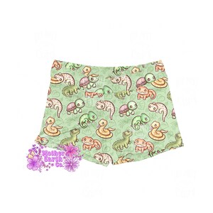 Op de afbeelding: Lichtgroene shorts met een herhaald patroon van cartoonreptielen, waaronder schildpadden, slangen en hagedissen. De shorts hebben een comfortabele pasvorm en zijn gemaakt van zacht materiaal. Het logo "Mother Earth Co." is ook zichtbaar.