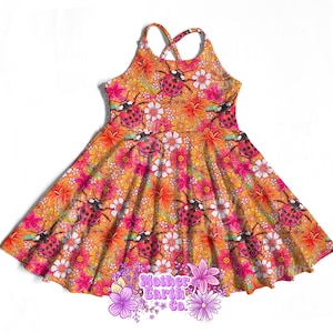 May include: A sleeveless dress with a vibrant floral and ladybug pattern. The dress features a crisscross back and a flared skirt. The color palette includes orange, pink, and white, creating a cheerful and playful design. The dress is suitable for children.