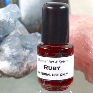 Op de afbeelding: Een klein, doorzichtig glazen flesje met een zwarte dop gevuld met een rode vloeistof. Het etiket vermeldt "Objets d'Art & Spirit Ruby EXTERNAL USE ONLY".