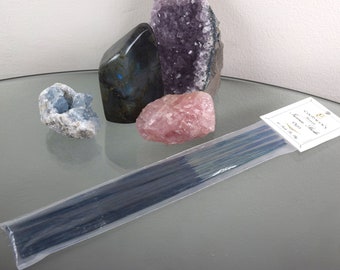 Può includere: Un pacchetto di bastoncini di incenso con un'etichetta bianca che recita "Garden's Essence Incense - Oud". Il pacchetto è su una superficie di vetro con diversi cristalli, tra cui un'ametista viola, un quarzo rosa e un cristallo blu.