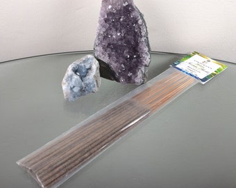 May include: A package of incense sticks with a label that reads "Cosmic Elements Incense - Mystique". The package is on a glass surface with two crystal clusters, one purple and one blue.