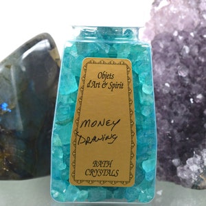 May include: A clear glass jar filled with teal blue bath crystals. The jar has a gold label that reads "Objets d'Art & Spirit" and "Money Drawing Bath Crystals".