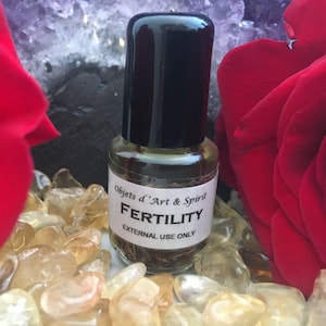 May include: A small glass bottle with a black cap filled with a clear liquid and herbs. The label reads "Objets d'Art & Spirit FERTILITY EXTERNAL USE ONLY".