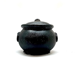 May include: A small black cauldron with a lid. The cauldron is made of ceramic and has a rustic, aged look.