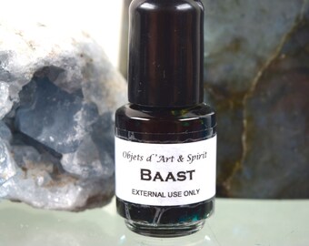 May include: A small glass bottle with a black cap and a white label. The label reads "Objets d'Art & Spirit" and "BAAST" in bold letters. The label also says "EXTERNAL USE ONLY".