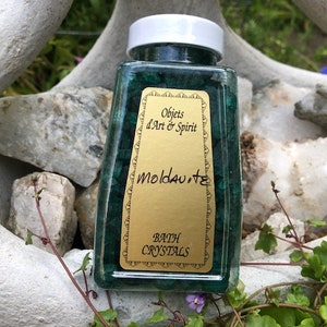 May include: A clear glass jar filled with green crystals labeled "Objects d'Art & Spirit Moldavite Bath Crystals".