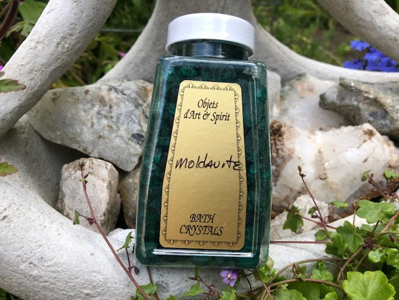 May include: A clear glass jar filled with green crystals labeled "Objects d'Art & Spirit Moldavite Bath Crystals".