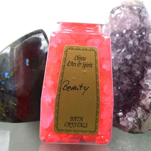 May include: A clear plastic jar filled with pink bath crystals. The jar has a gold label that reads "Objets d'Art & Spirit" and "Beauty" in a cursive font. The label also says "Bath Crystals".