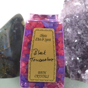 May include: A clear glass jar filled with pink and purple bath crystals. The jar has a gold label that reads "Objets d'Art & Spirit" and "Black Tourmaline Bath Crystals".