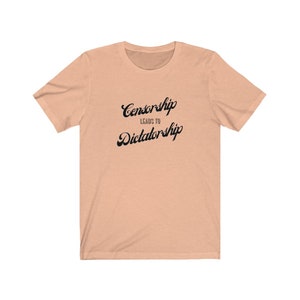 May include: A peach-colored t-shirt with the text "Censorship Leads to Dictatorship" printed in black.