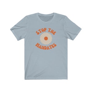 May include: Light blue t-shirt with a daisy graphic and the text "STOP THE MANDATES" in orange.