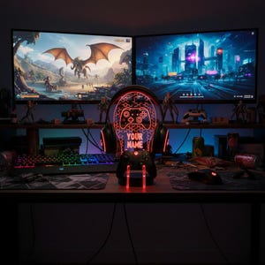 May include: A gaming setup featuring two monitors displaying game scenes. A headset-shaped LED light with a controller graphic and the text "YOUR NAME" is in the foreground. A keyboard, mouse, and controller are also visible.