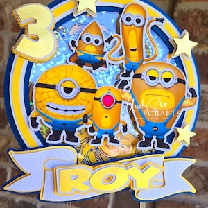 May include: A yellow and blue Minion themed cake topper with a number 3, the word "ROY", and several Minion characters.