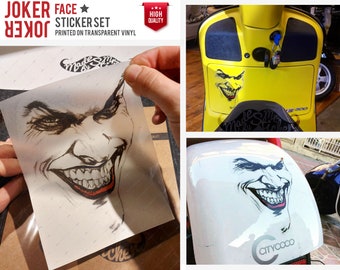 May include: A sticker set featuring a Joker face with a menacing grin. The sticker is printed on transparent vinyl and is shown being applied to a yellow scooter.