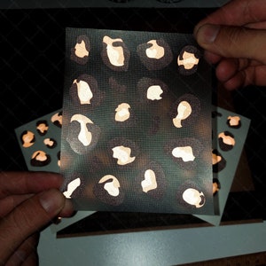 May include: A sheet of clear vinyl with a gold glitter leopard print design. The sheet is being held by two hands. The text "Made by Mr. Sticker" is visible in the background.