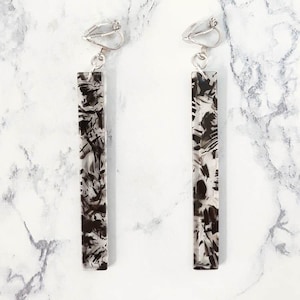 Peut inclure: Une paire de longues boucles d'oreilles clips argentées avec des motifs abstraits noirs et blancs. Les boucles d'oreilles sont de forme rectangulaire et ont un look élégant et moderne.