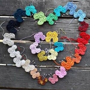 Könnte beinhalten: Eine Sammlung gehäkelter Schmetterlinge in verschiedenen Farben, die in Herzform auf einer Holzoberfläche angeordnet sind.