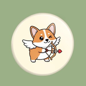 May include: A cartoon illustration of a corgi dog with angel wings and a bow and arrow with a heart-shaped tip. The corgi is orange and white, winking, and set against a cream-colored circle on a green background.