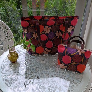 May include: Two tote bags with floral patterns. The larger bag is black with pink, red, and purple flowers. The smaller bag is a similar pattern but in a smaller size.