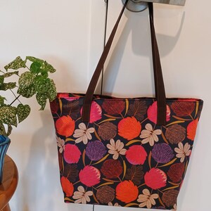May include: A brown tote bag with a floral print featuring pink, orange, and purple flowers on a dark background. The bag has brown straps.