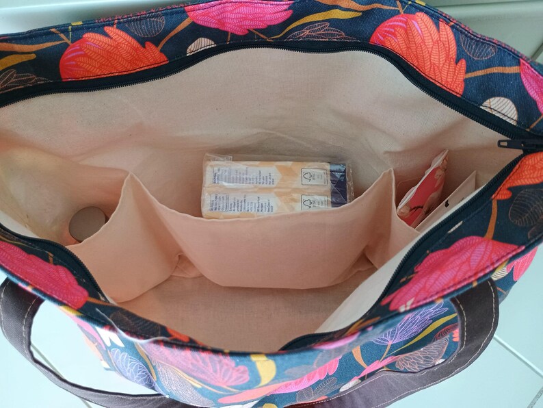 May include: A black tote bag with a floral print featuring pink, orange, and yellow flowers. The bag has a zipper closure and multiple interior pockets. The bag is lined with a beige fabric.