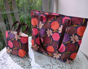 May include: Two tote bags with floral patterns. The larger bag is navy blue with pink, orange, and purple flowers. The smaller bag is red with pink, orange, and purple flowers.