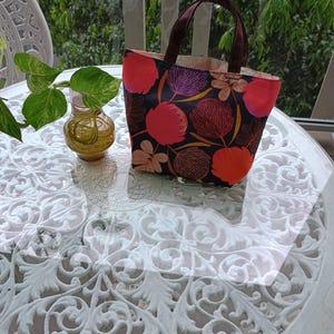 May include: A small, black tote bag with a floral print featuring pink, red, and purple flowers. The bag has brown handles and a white lining.
