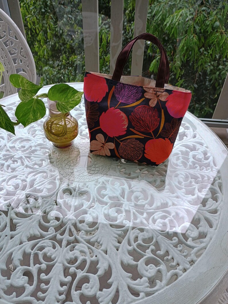 May include: A small, black tote bag with a floral print featuring pink, red, and purple flowers. The bag has brown handles and a white lining.