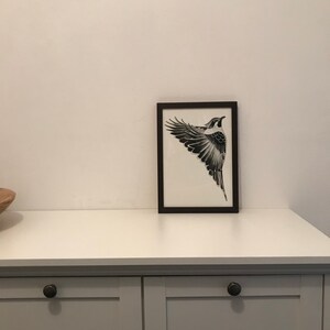 以下が含まれることがあります： 白い棚に飾られた、黒い額縁に入った、飛んでいる鳥の白黒の絵