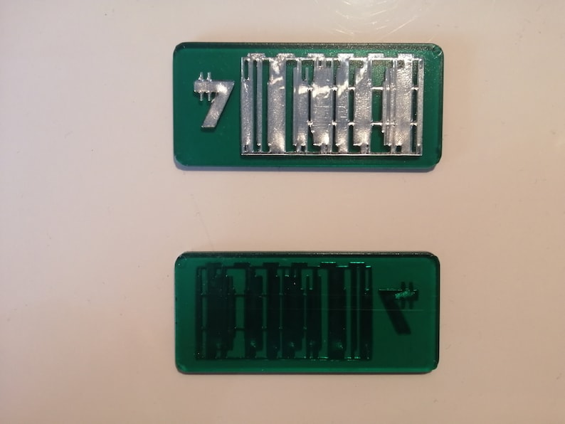May include: Two rectangular, emerald green objects with silver metal detailing. The top object has the number 7 and a series of vertical bars. The bottom object has a similar design, but in a darker green.