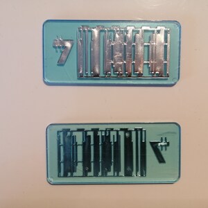 May include: Two rectangular, light blue plastic molds with silver metal components. Each mold has the number "7" in the corner. The metal components appear to be small, rectangular shapes.