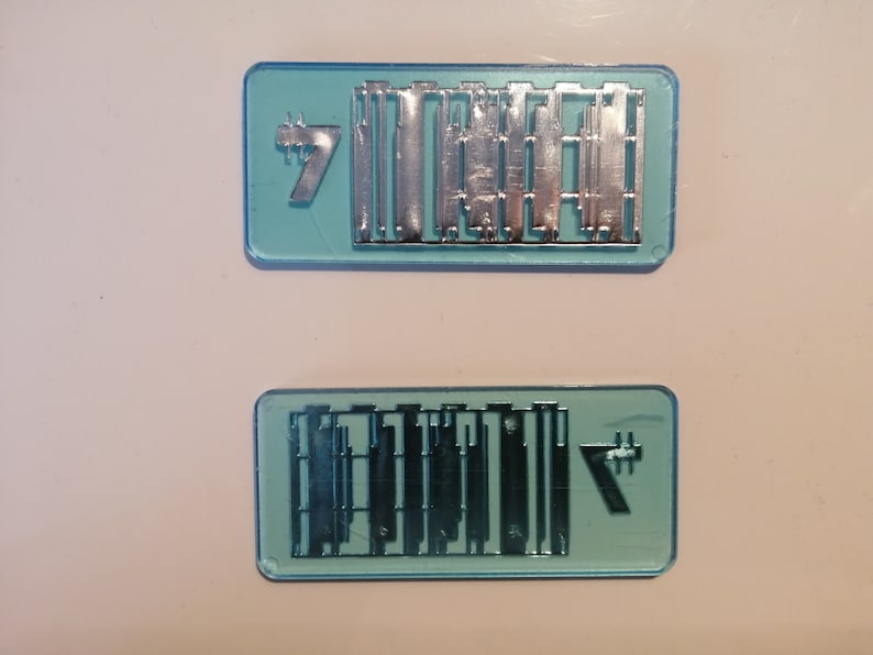 May include: Two rectangular, light blue plastic molds with silver metal components. Each mold has the number "7" in the corner. The metal components appear to be small, rectangular shapes.
