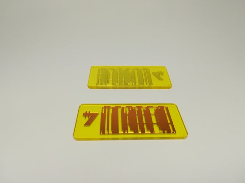 May include: Two yellow rectangular acrylic pieces with etched designs. The top piece has a series of vertical lines and a symbol. The bottom piece has the number 7 and a similar design in a copper color.