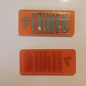 May include: Two orange rectangular objects with silver metal detailing. One has the number 7 and a series of vertical lines. The other has a mirrored image of the lines and the number 7.